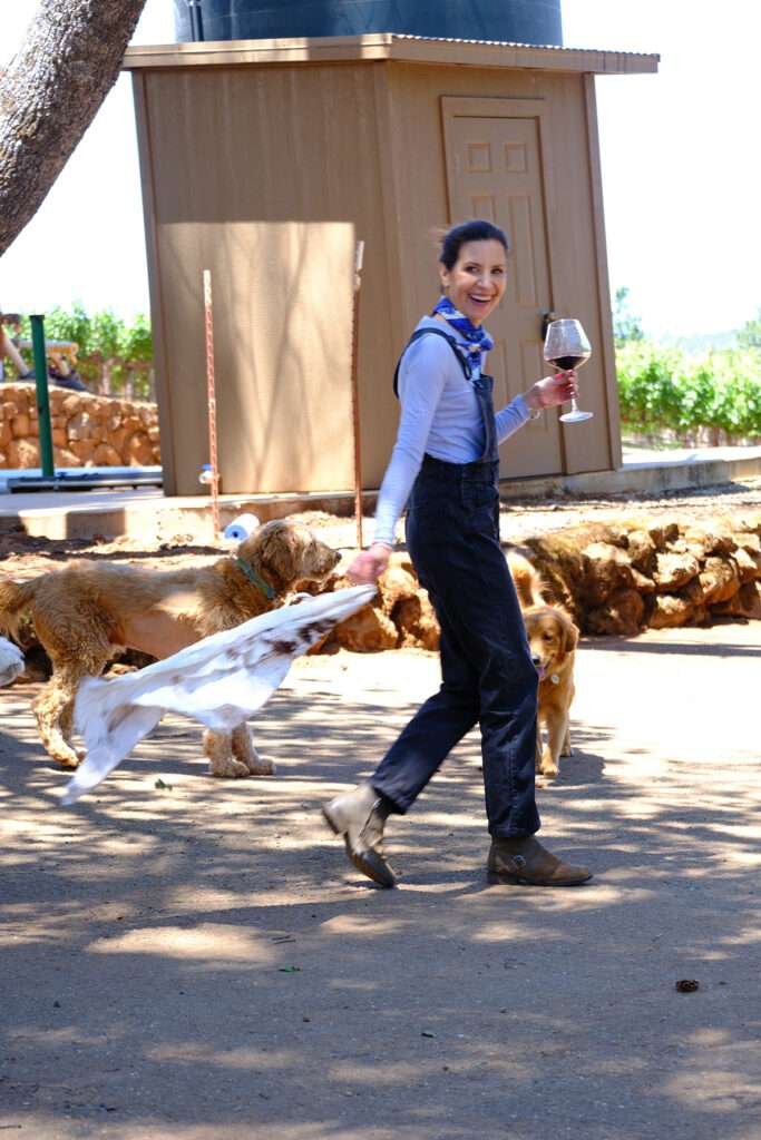 a woman walking a dog while holding a glass of wine.